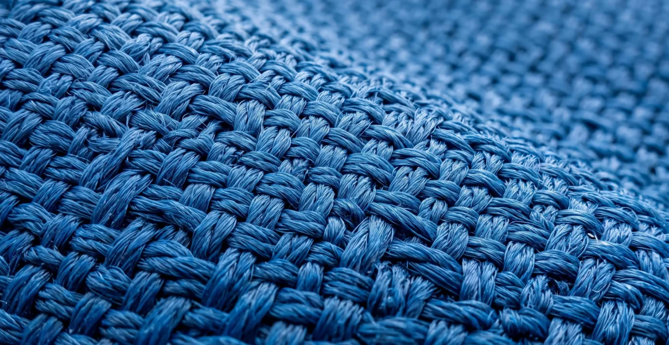 Fotografía macro extrema mostrando la estructura entrelazada de fibras acrílicas de una lona técnica para toldo, con profundidad de campo reducida y fondo desenfocado neutro